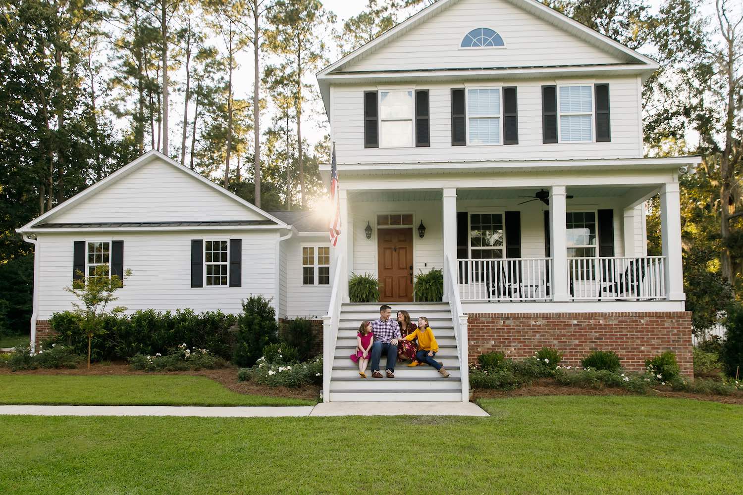Family of Four With Daughters Sitting on the Steps Outside Their their Home Laughing Together